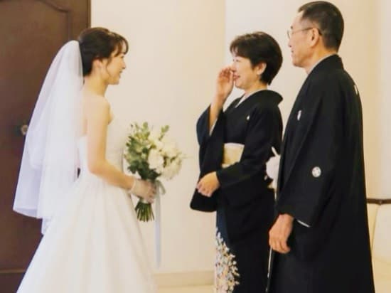 親御様向け婚活のイメージとして結婚式でウェディングドレス姿の娘を見つめる黒留袖と紋付羽織袴姿の父親と母親