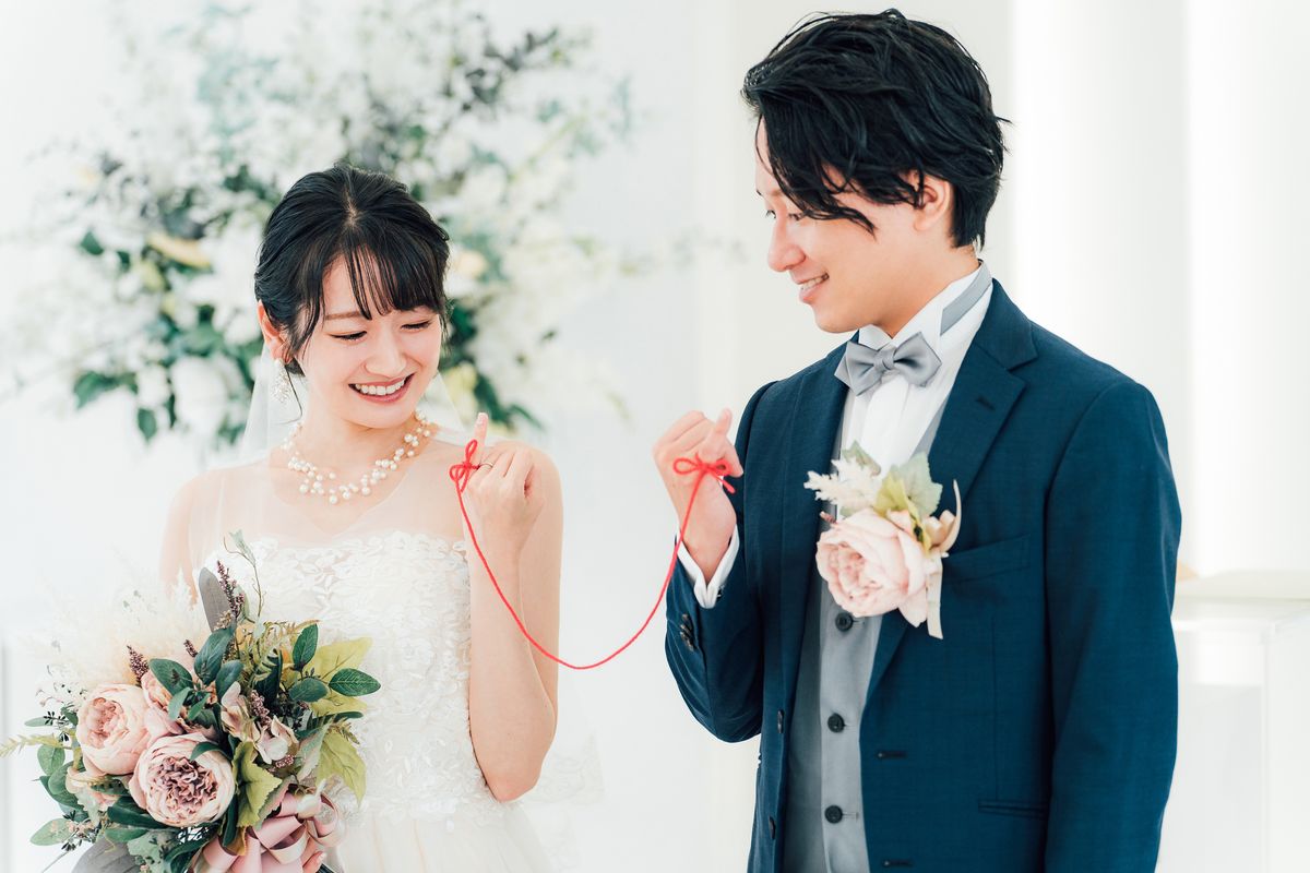 小指に結んだ赤い糸を見せ合って微笑む新郎新婦