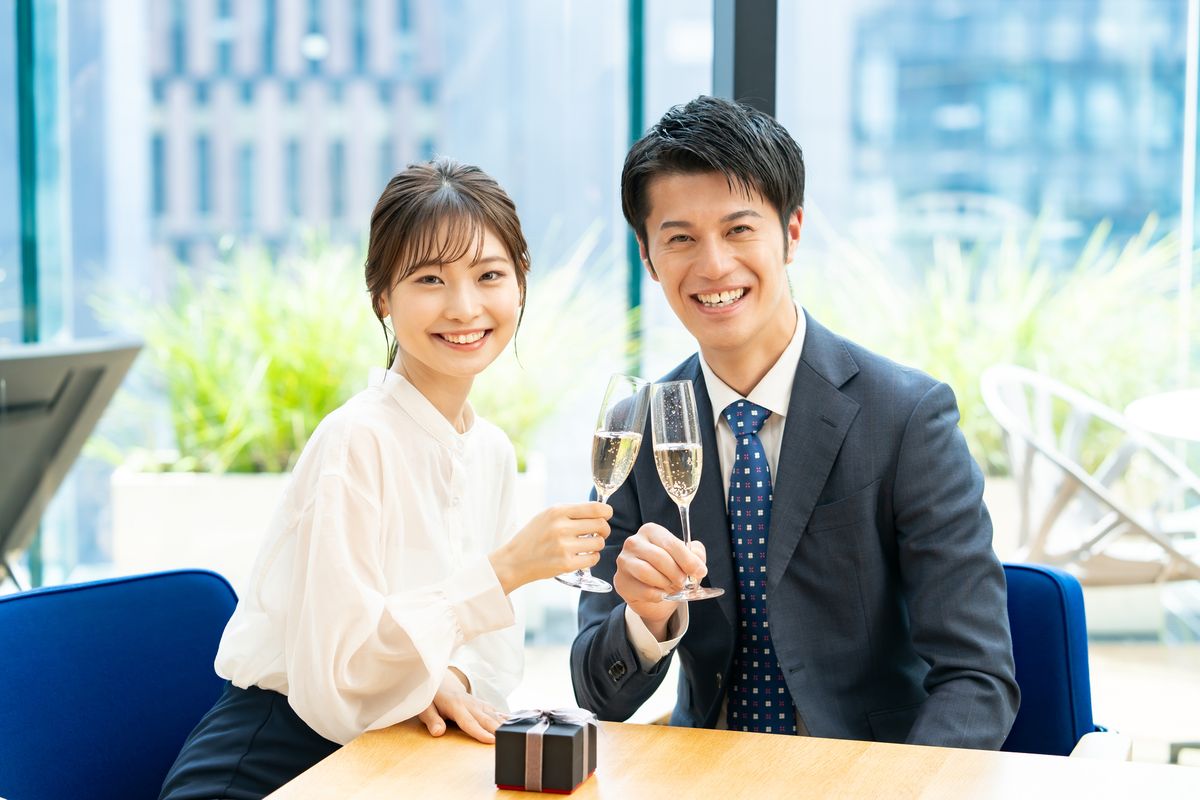 スーツ姿の男性とブラウス姿の女性が、グラスを手に笑顔を見せる