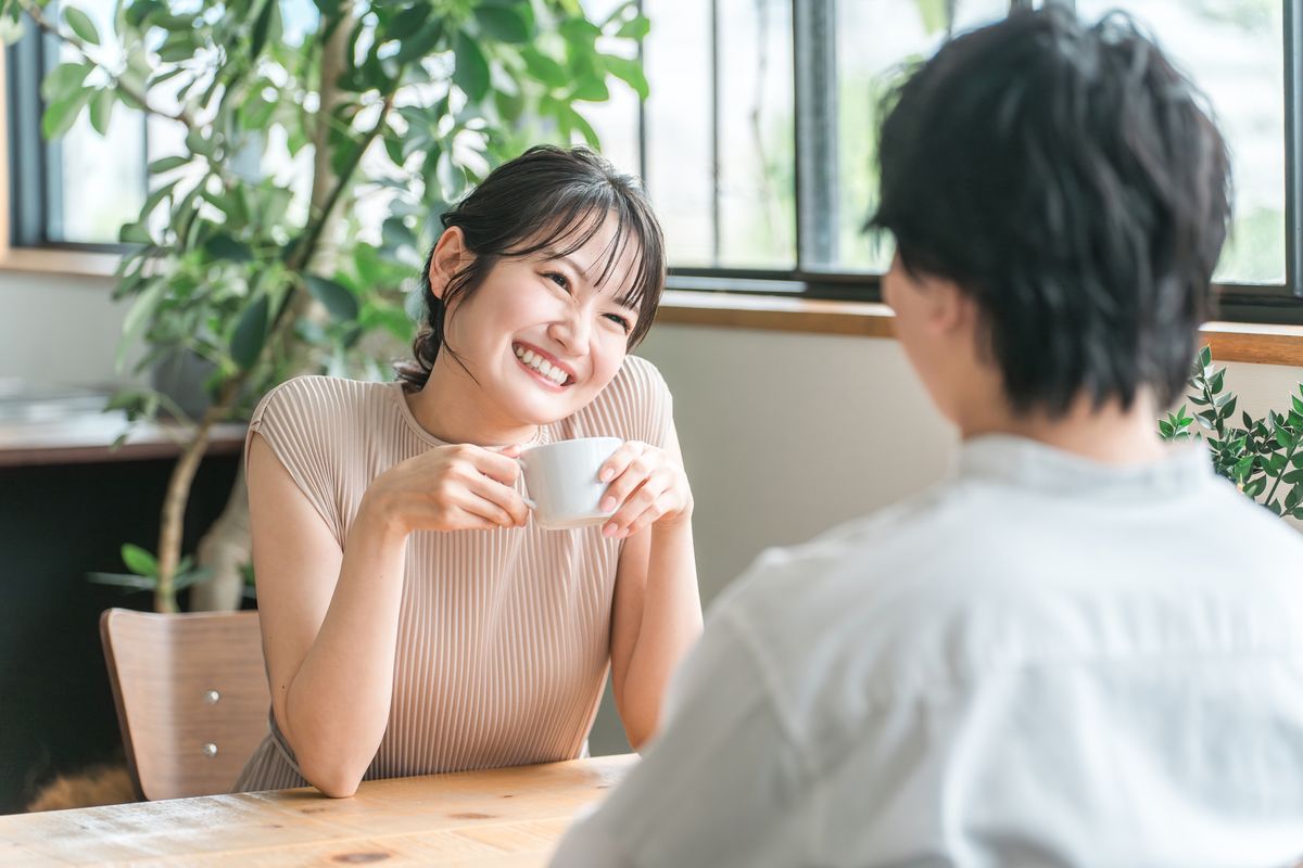 カフェで、向かいの男性と話して笑顔を見せる女性