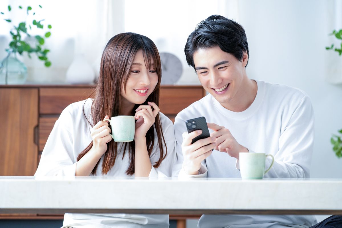 並んで座り、スマートフォンの画面を一緒に見て笑う男性と女性